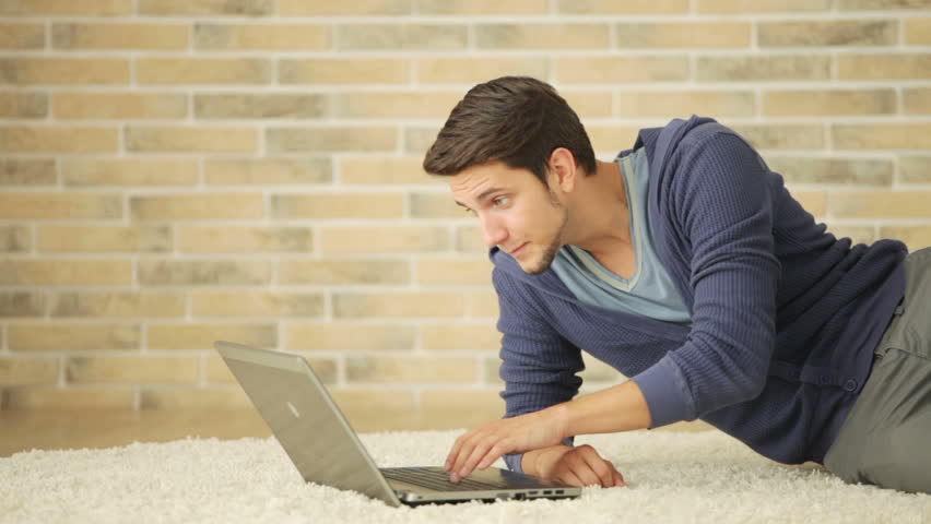 Charming guy sitting on floor and using laptop