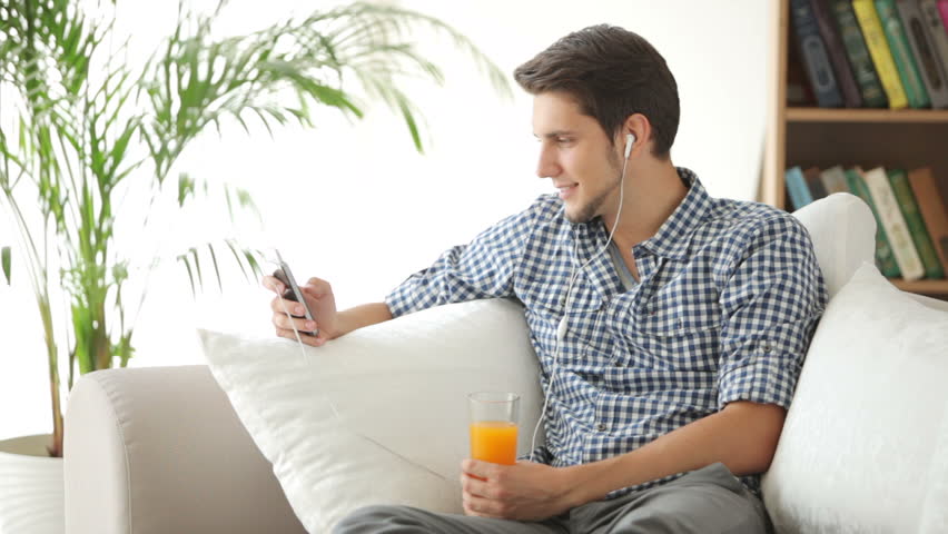 Charming guy sitting on sofa and listening to music with earphones