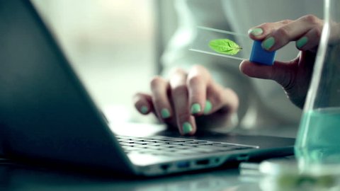Biologist examine plant leaf and writing results on laptop
