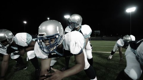Close up steadicam shot of a football team in a huddle and rushing to the line