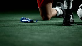 A soccer player kneels down and ties his cleat, close up