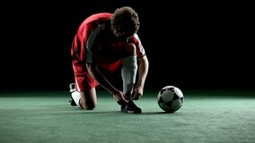 A soccer player kneels down and ties his cleat