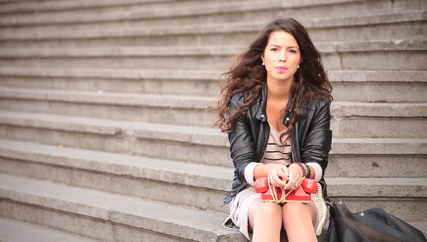 Attractive young adult brunette curly woman dialing and speaking on vintage obsolete phone or telephone. Business communications idea and concept.
