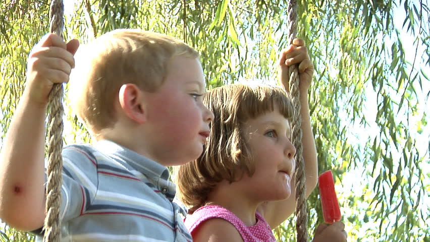 Two children sitting on a swing eating popsicles