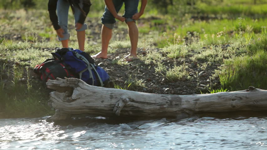 Backpackers roll up pants and put feet in stream
