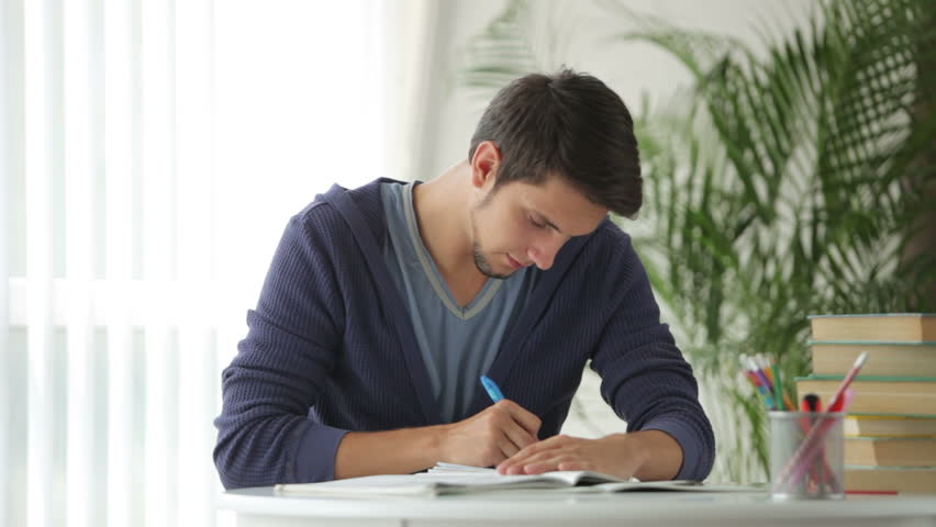 Male student sitting at table and writing in notebook
