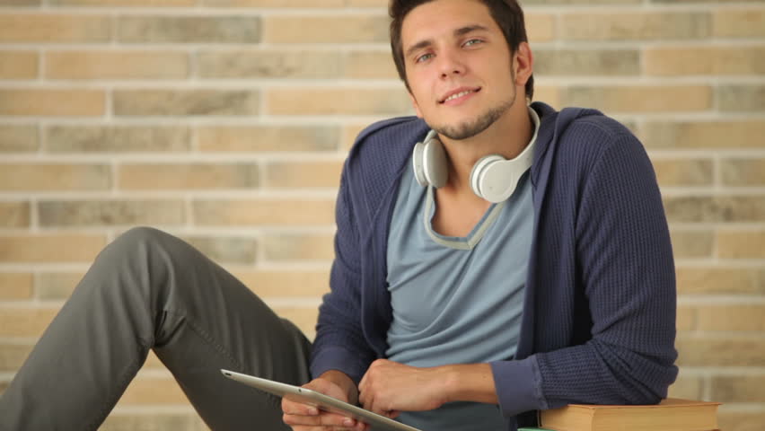 Handsome young man sitting on floor with books and using touchpad
