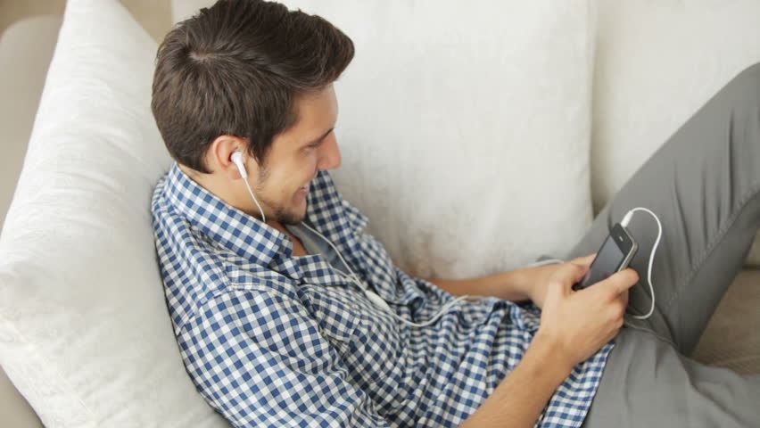 Good-looking man relaxing on sofa and listening to music with earphones