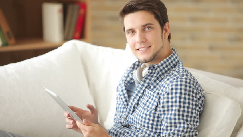 Good-looking guy sitting on sofa and using touchpad