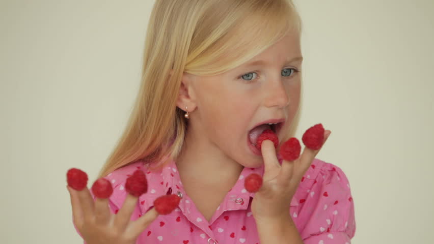 Pretty little girl eating raspberries from top of her fingers and smiling