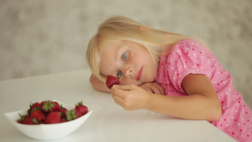 Sleepy little girl sitting at table and eating strawberries