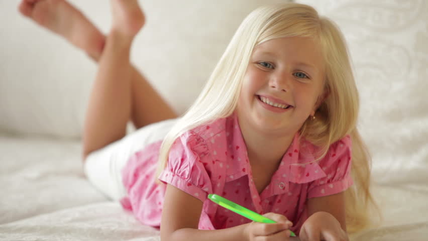Happy little girl lying on sofa writing in notebook and smiling