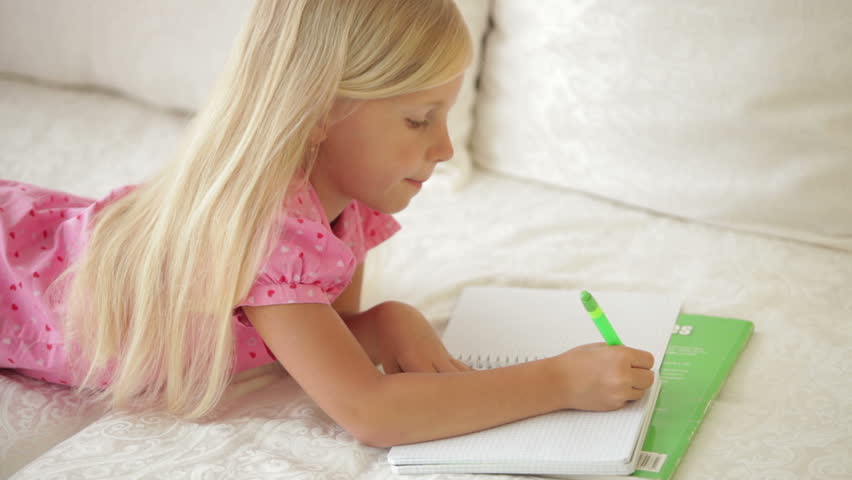 Smiling little girl lying on couch and writing in notebook