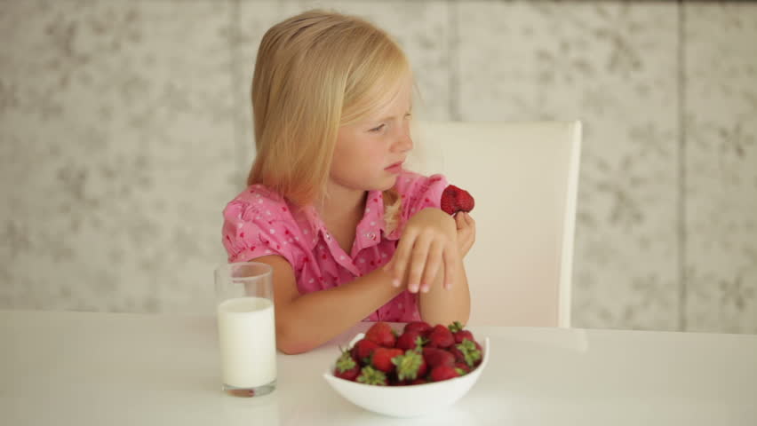 Funny little girl sitting at table and eating strawberries