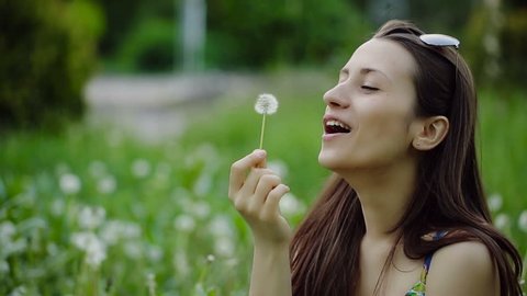 Young Woman Blowing Dandelion and Laughing on a Summer Field