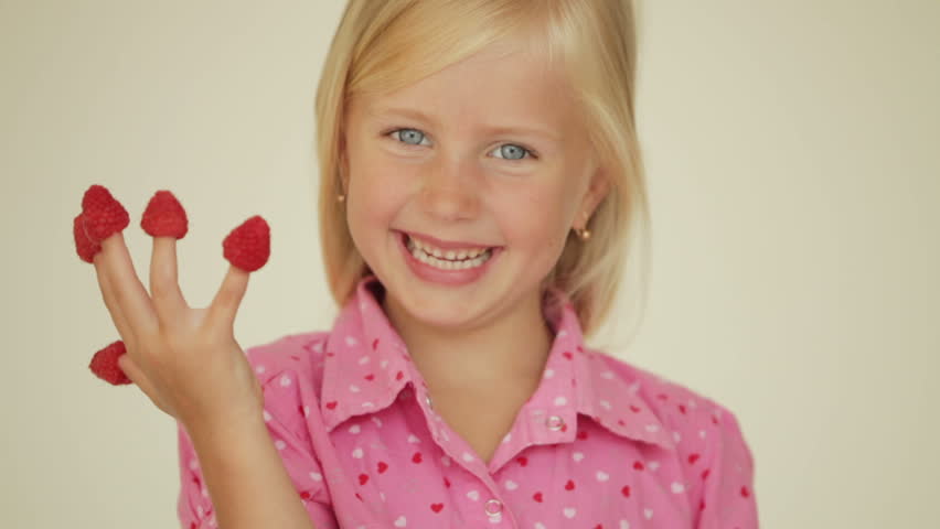 Smiling little girl eating raspberries from top of her fingers
