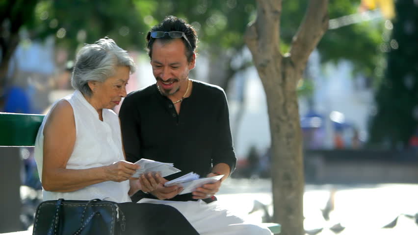 An older lady and a man sit on a bench and look at pictures