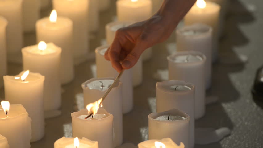 A Female Hand Lighting Up White Candles Aligned Vertically With Wooden Stick.