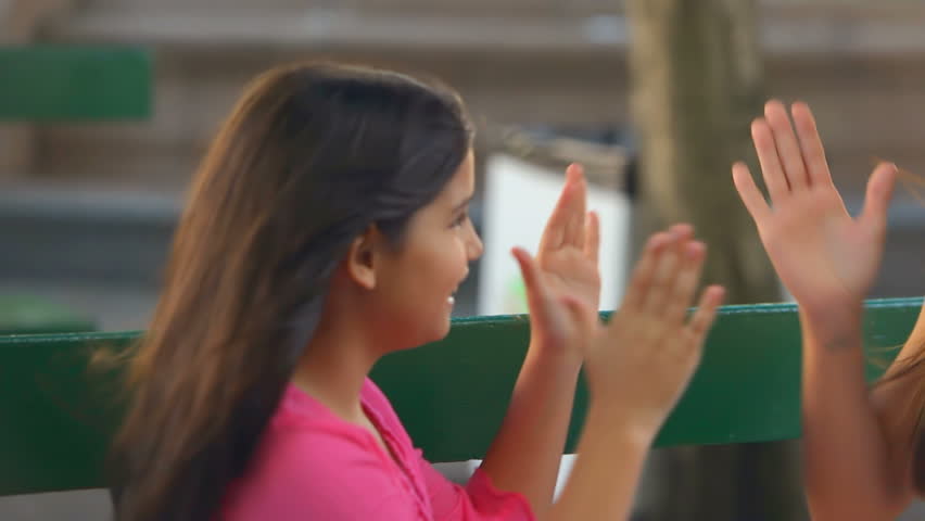 A mother and daughter sit on a bench and play hand games