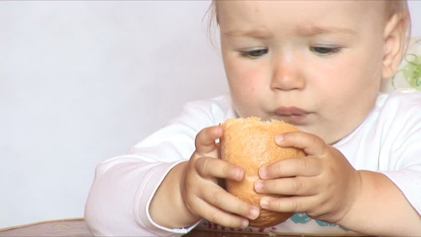 Small child eats bread behind a table