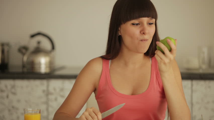Charming girl sitting at kitchen table peeling and eating kiwi fruit