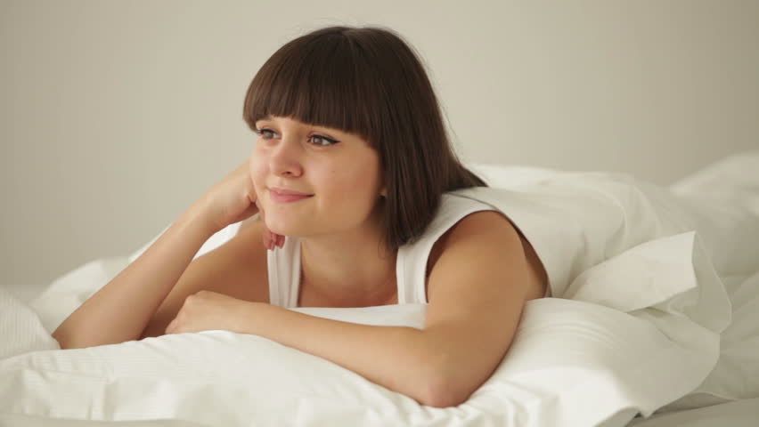 Attractive girl relaxing in bed looking at camera and smiling