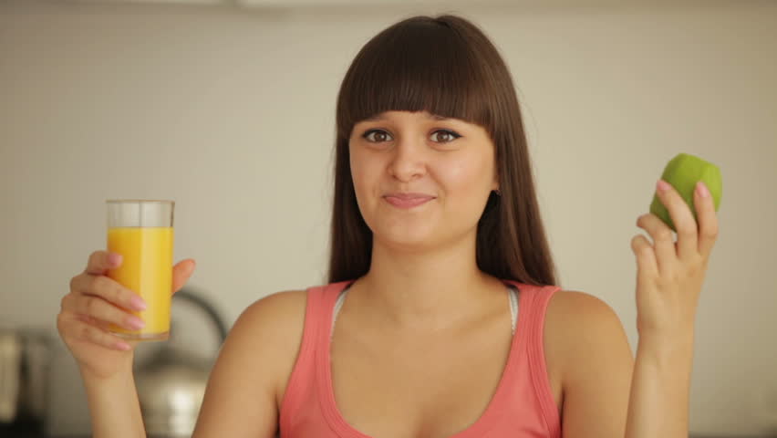 Beautiful girl at kitchen holding glass of juice and eating kiwi