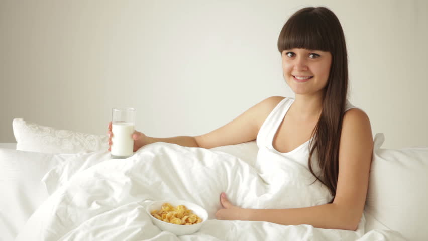 Attractive girl relaxing in bed drinking milk and eating cereal