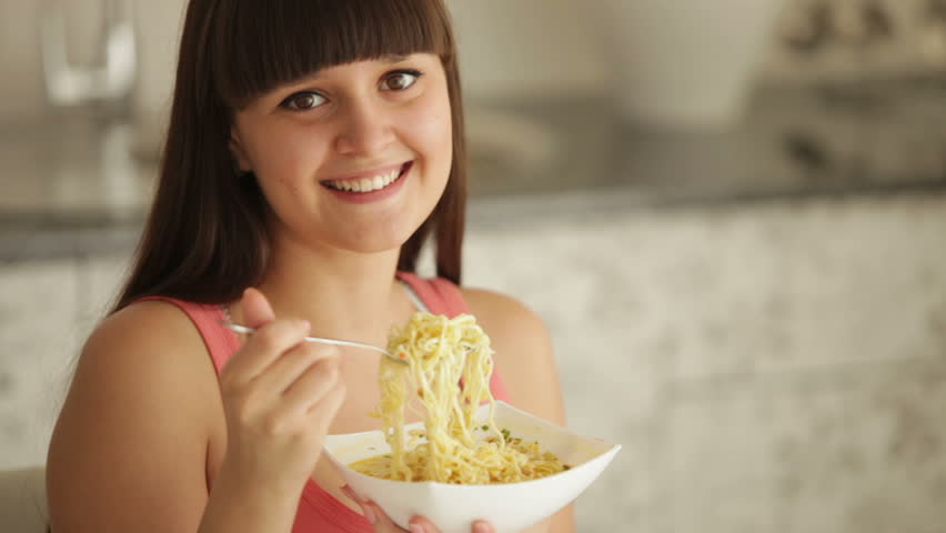 Charming girl at kitchen eating noodle and smiling