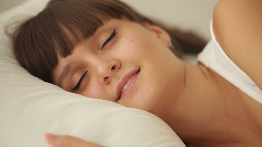 Beautiful girl sleeping in bed waking up and smiling at camera