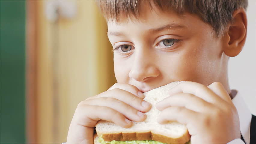 Little schoolboy eating sandwich in class