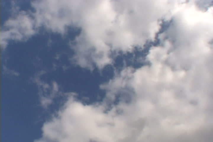 Airplane flying high in clouds on sunny day.