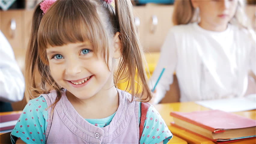 Little schoolgirl sitting behind desk during lesson in school