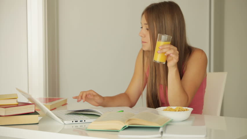 Charming girl studying at table and drinking juice