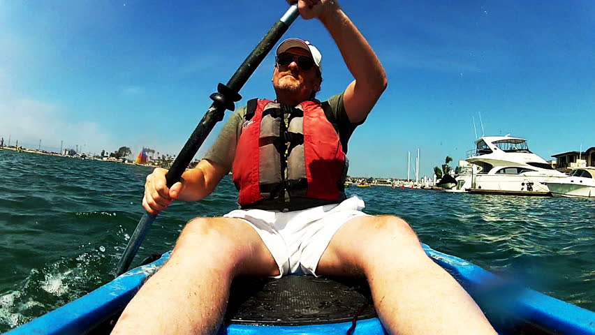 A middle aged or mature man paddles a kayak past yachts and pleasure boats in