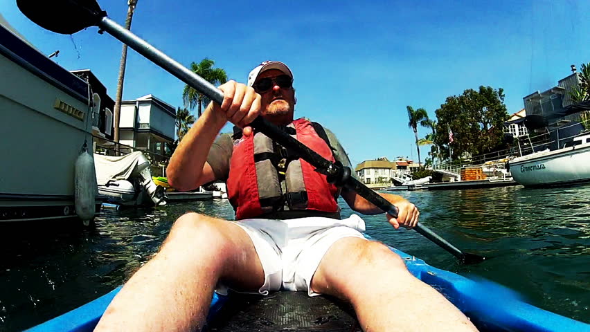 A mature or middle aged man is paddling a kayak or kayaking in the Naples Island