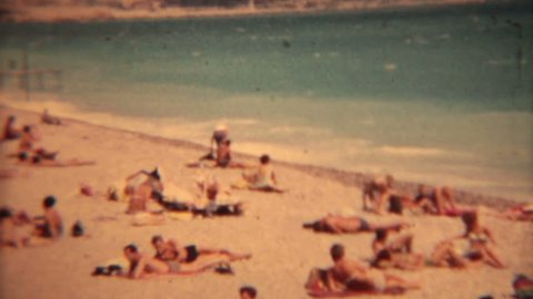LES BAINS EUROPE CIRCA 1963: Lido Les Bains Beach bikinis vintage film. People on beach,surf boards, swimsuits and bikinis. Men in Speedo wear. Travel and fun historical view.