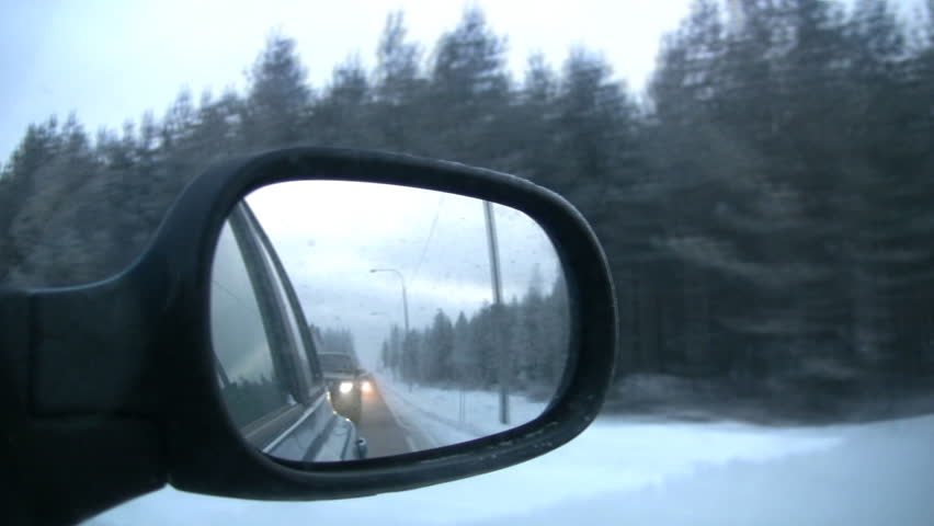 Kind on a snow-covered pine wood in the right mirror of the moving car.