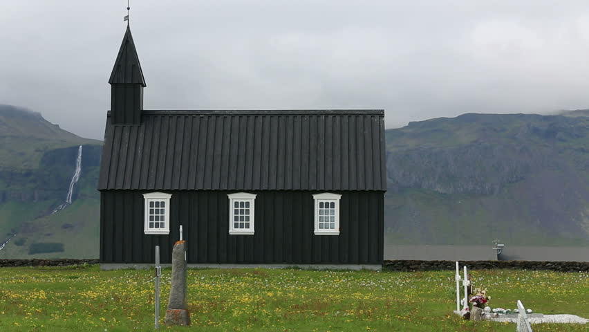 Black wooden church in front of a mountain range in Budir, Iceland