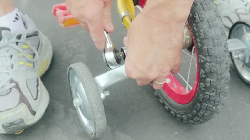 A father putting training wheels on his child's bike