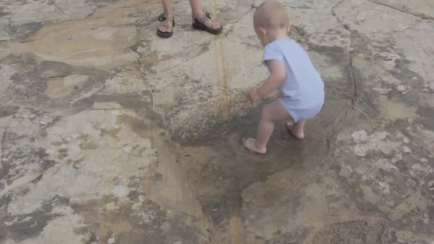 A baby boy playing in a puddle on the desert rock