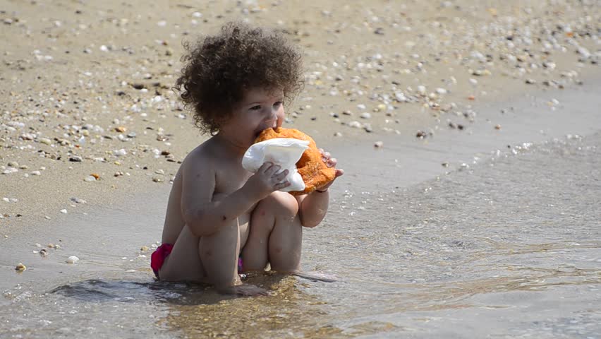 Beautiful hungry child is sitting relaxed on the summer beach eating a fresh