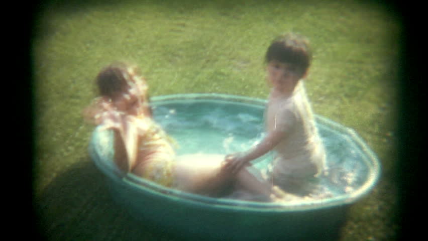 A brother and sister play in a baby pool outside.   Vintage 1970s film transfer.