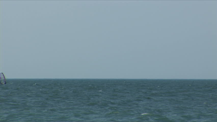 Sailboard in a sea bay. Zoom out.