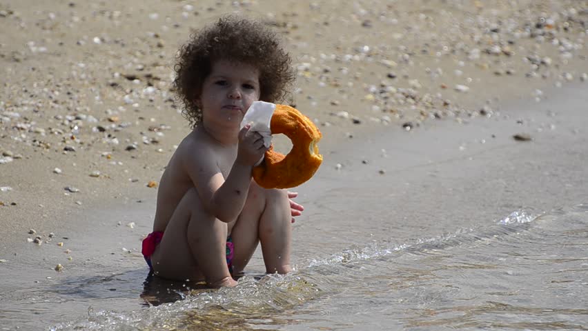 Beautiful hungry child is sitting relaxed on the summer beach eating a fresh