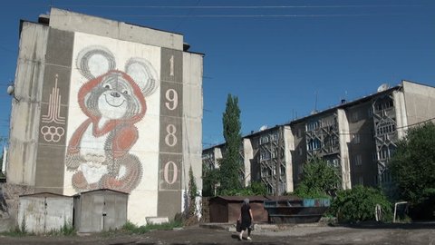 OSH, KYRGYZSTAN - 30 JUNE 2013: People walk past an old Soviet apartment building, with an advertisement of the 1980 Olympic Games on it, in Osh, Kyrgyzstan