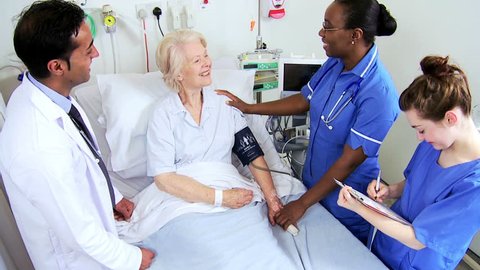 Caring health care providers moniter vital signs of an elderly female hospital patient