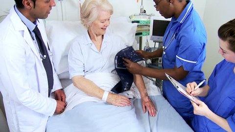 Elderly female patient having blood pressure taken at bedside by multi ethnic medical team