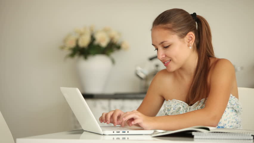 Pretty girl sitting at table studying with laptop looking at camera and smiling.