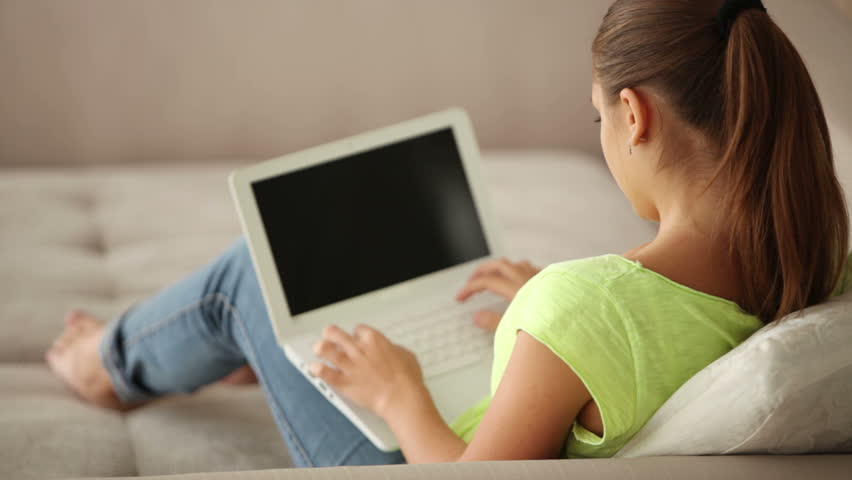 Pretty brunette girl sitting on sofa and using laptop